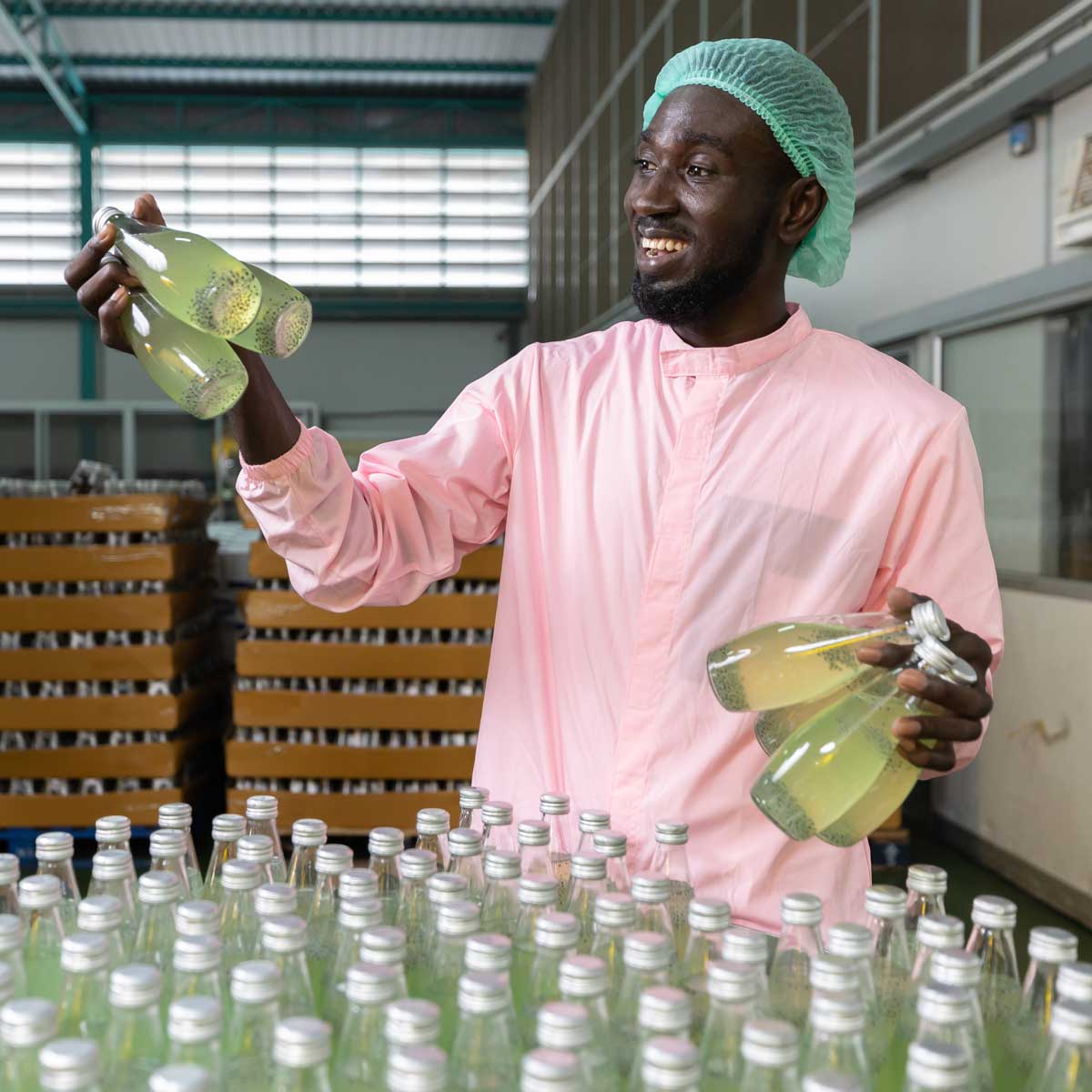 African male factory worker picking up and holding green juice bottle